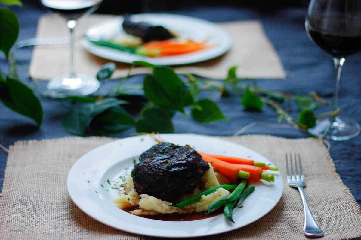 Beef cheek meal from the perspective of someone sitting down to eat. Another plate set up opposite.