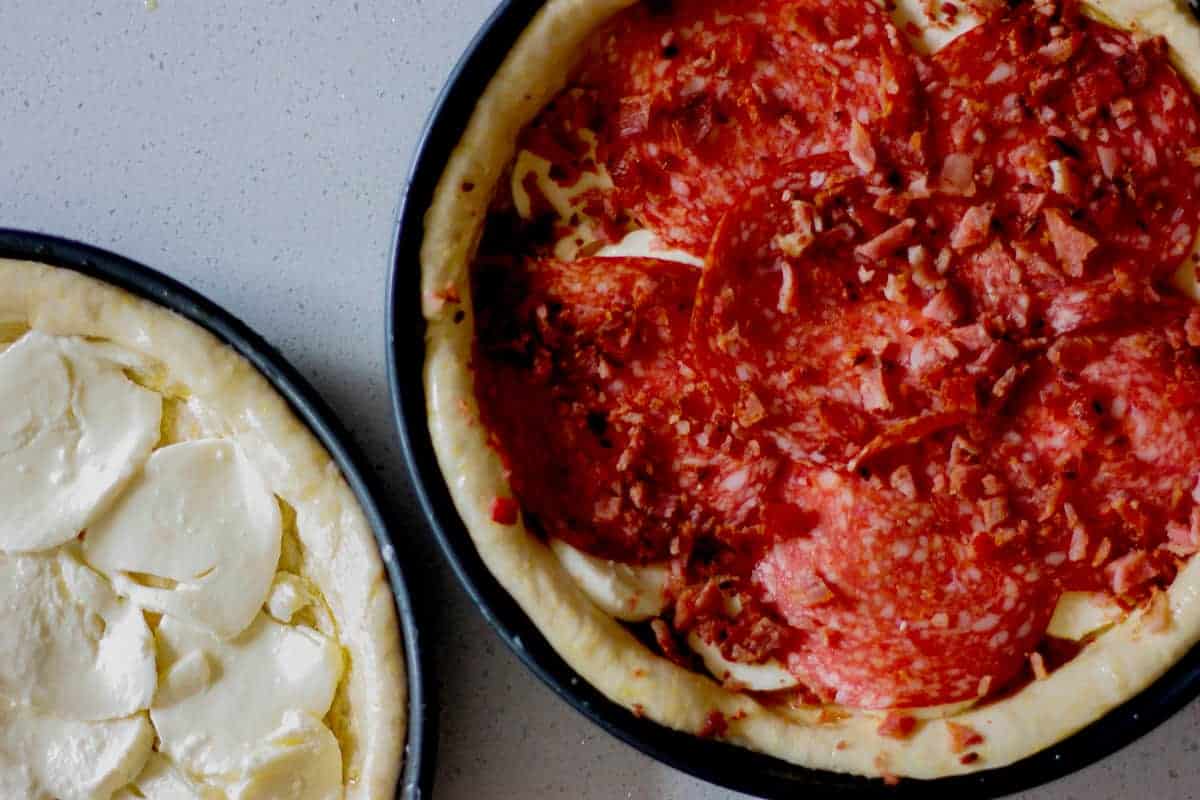 Two Chicago Pizzas in cake pans - one with mozzarella layer, the other with bacon bits and pepperoni as well.