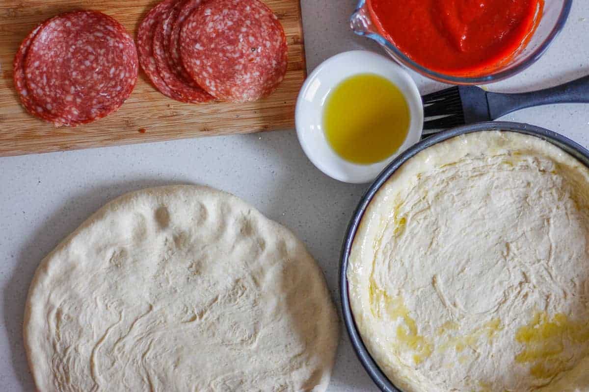 Two Chicago Pizza bases - one lining a cake tin, the other on a work surface with fillings set around them.