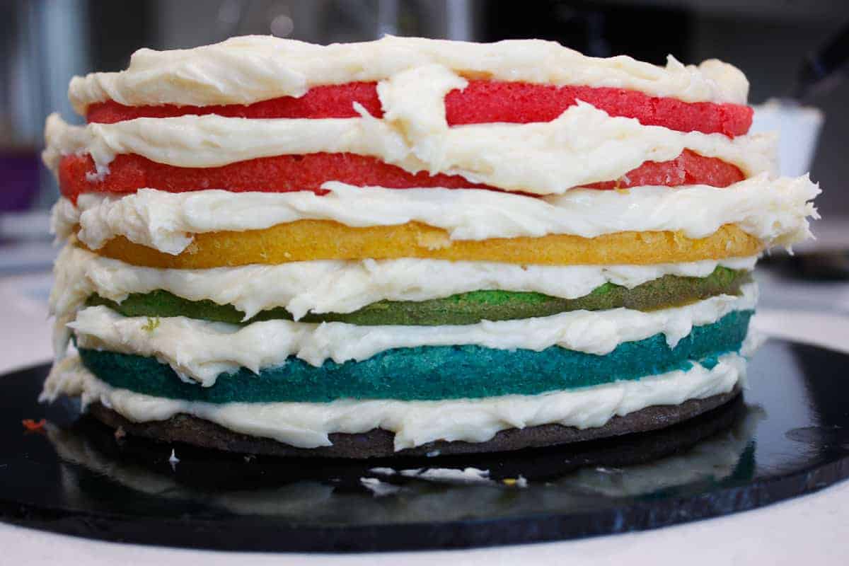 Six thin layers of coloured cake in a stack with frosting inbetween and on top.