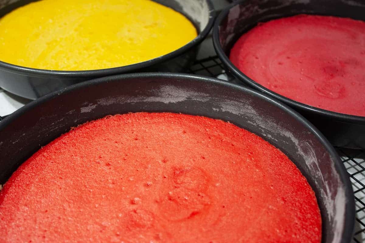 Yellow, red and orange baked cakes in their tins set on a cooling rack.