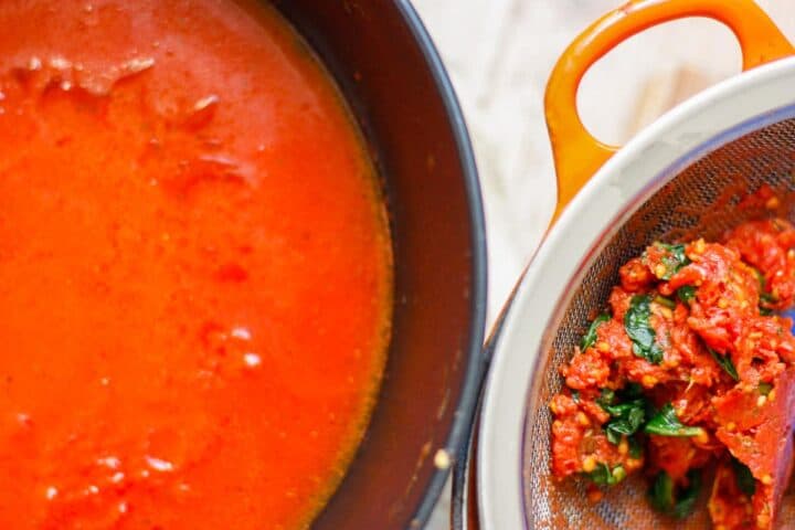 Strained tomato sauce in a black bowl next to the sieve containing strained product.