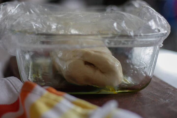 Freshly made dough in an oiled glass dish covered in a shower cap.