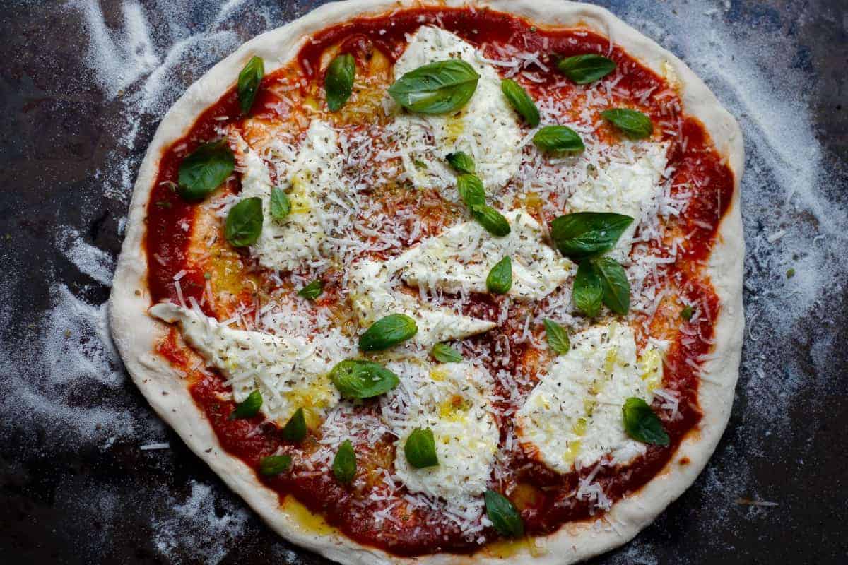 Oven-ready margherita pizza atop a semolina-dusted baking sheet.