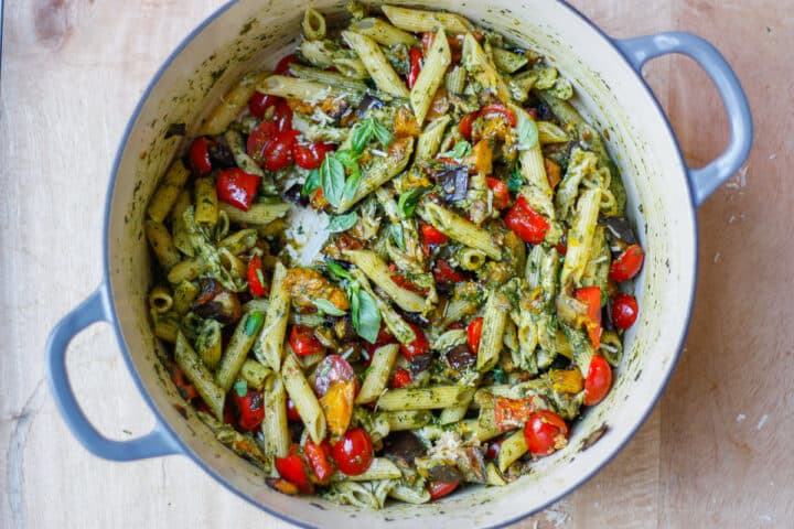 Looking down into a massive pot of completed pasta dish. Pops of red from the cherry tomatoes and red capsicum.