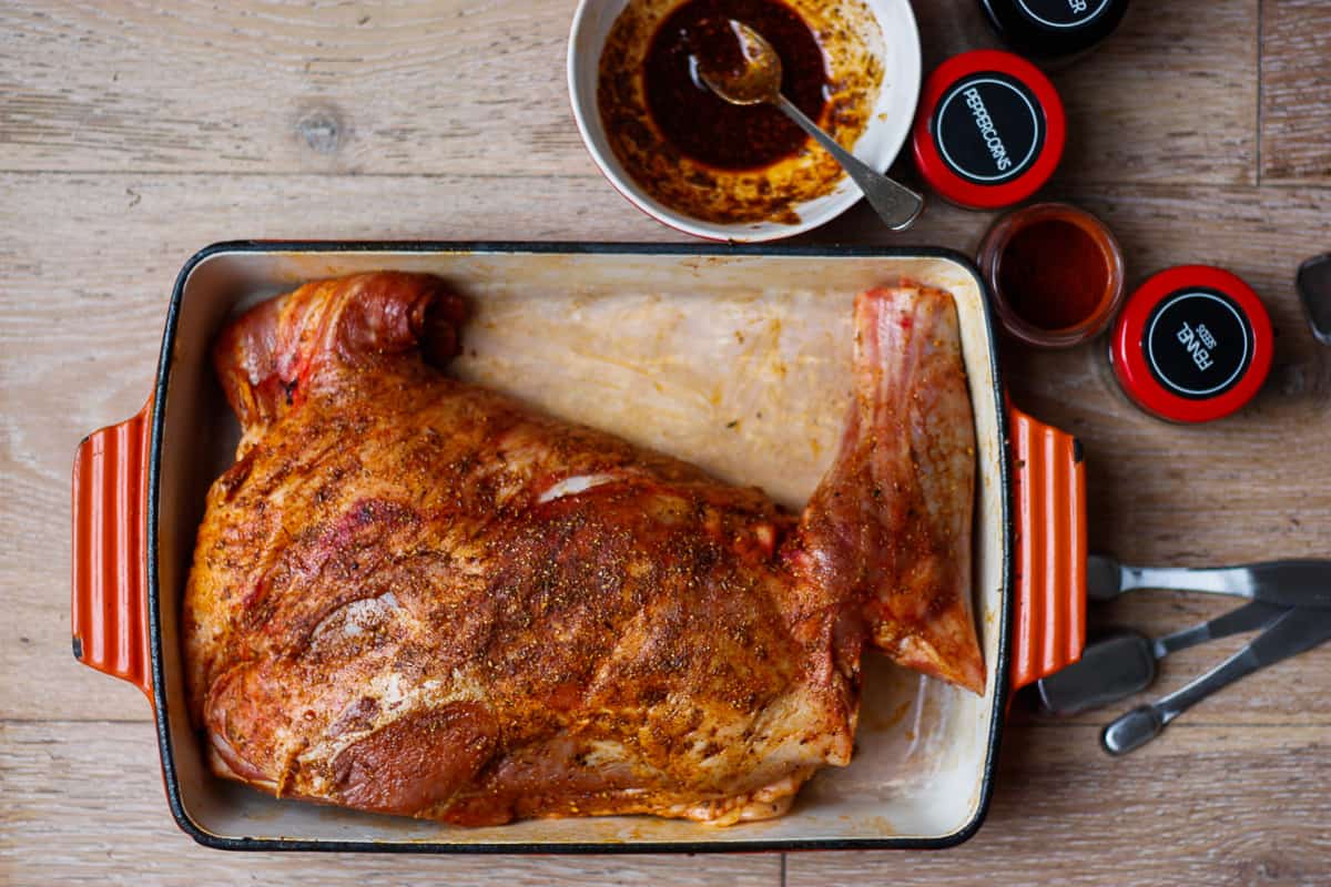 Top view of whole lamb shoulder bronzed with spice rub in a baking dish.