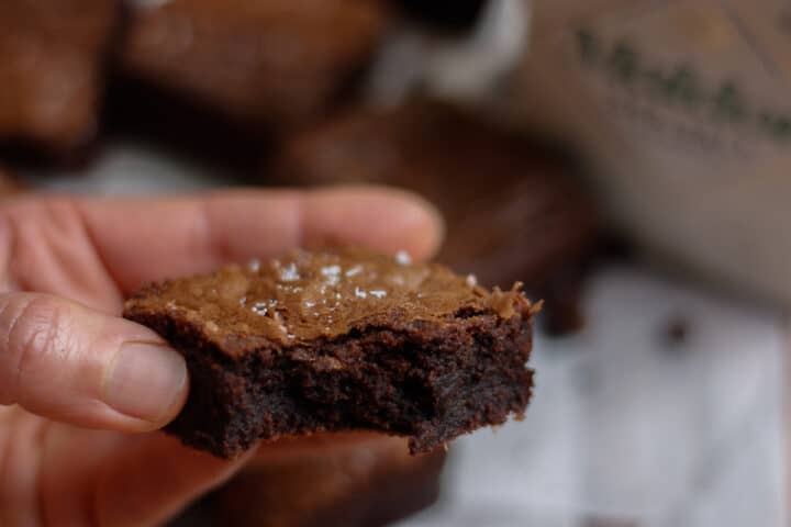 Single brownie held in a hand with a bite taken out of it.