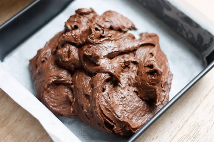 Mound of brownie batter in a lined pan ready for smoothing out and going in the oven.