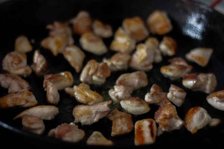 Bite-size pieces of browned chicken in a pan.