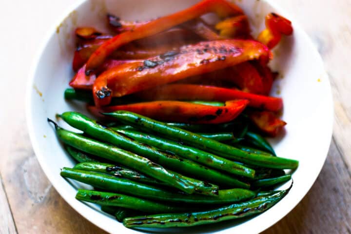 Charred strips of whole green beans and sliced capsicum in a white bowl.