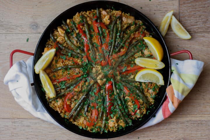 Cooked paella in a pan garnished with lemon wedges and chopped parsley.