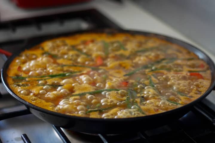 Pan of bubbling stock with some vegetables laying on the top.