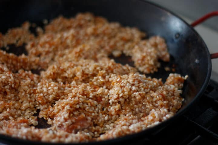 Dry rice coated in tomato paste in a pan.