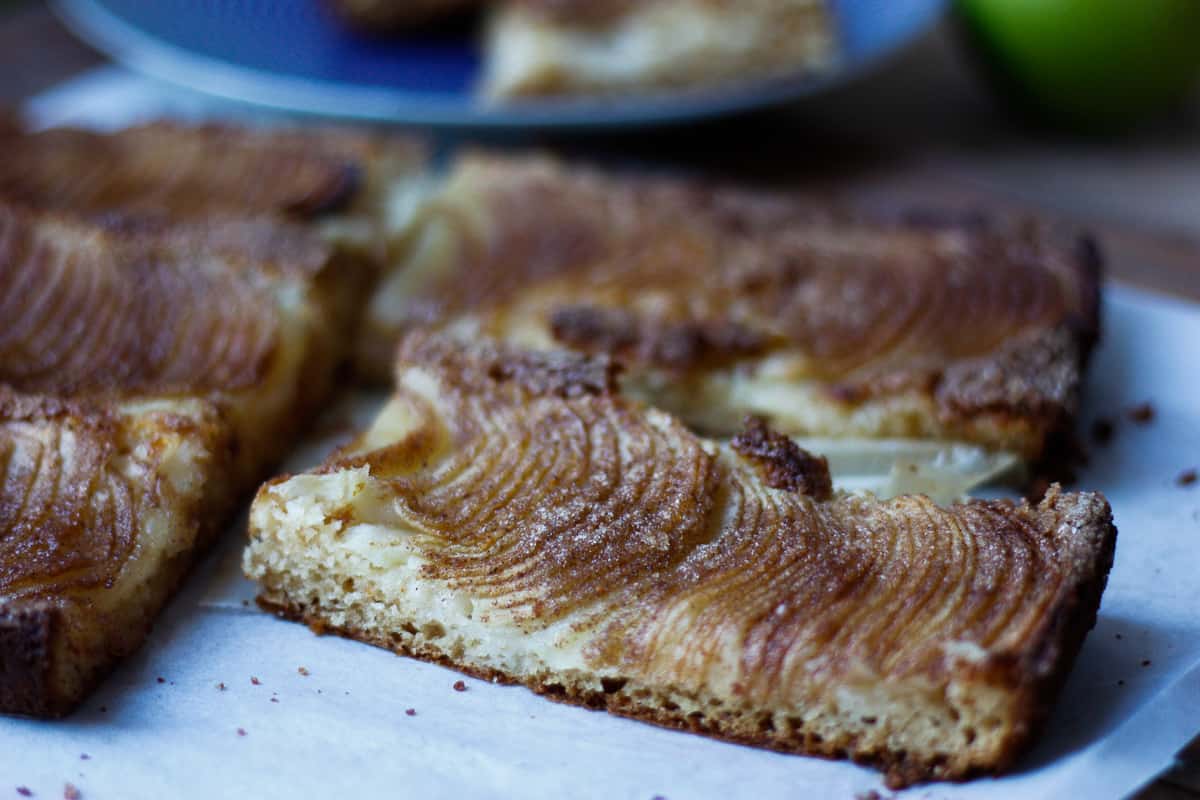 Side view of a rectangular piece of apple cake showing the thin cake and very thinly sliced apples on top.