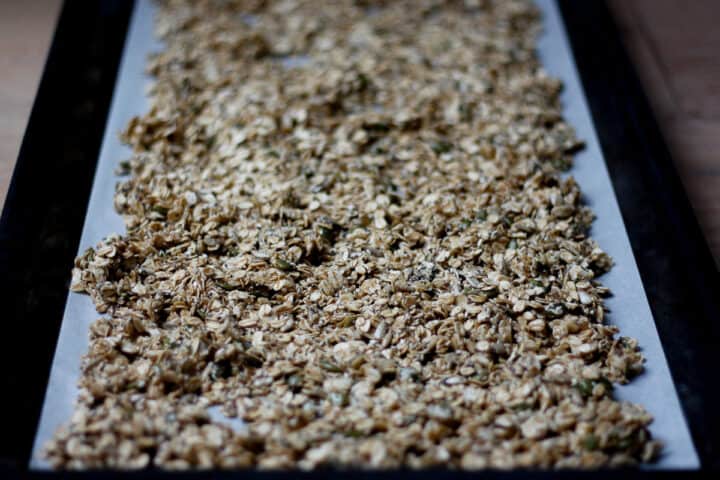 Raw granola spread out on a lined baking sheet ready to bake.