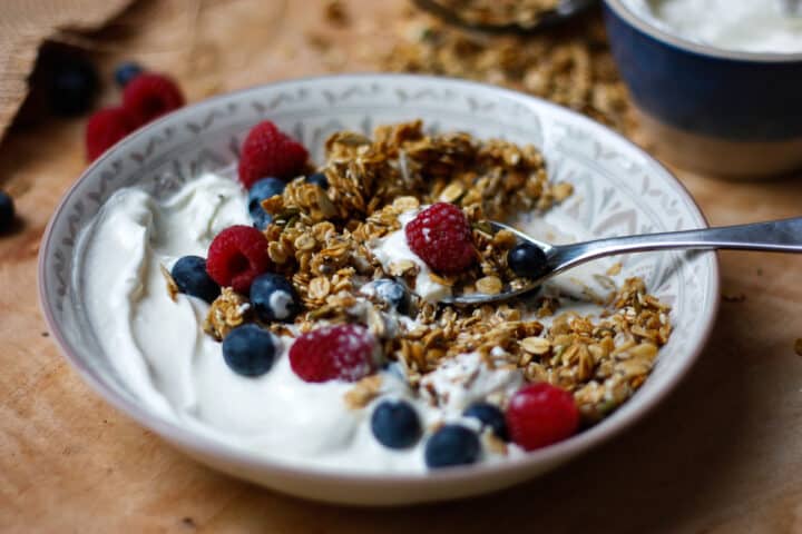 Granola served in a bowl with plain yoghurt and fresh berries.