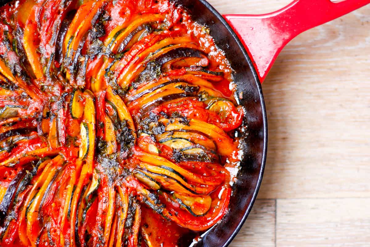 cooked ratatouille tian in a cast iron pan with a red handle.