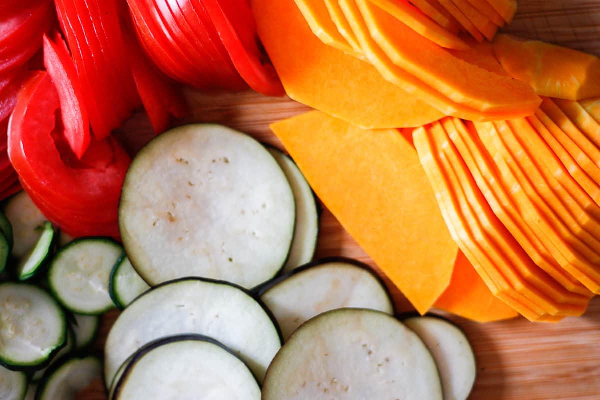 Thinly sliced pumpkin, tomato, eggplant and zucchini rounds on a wooden board.