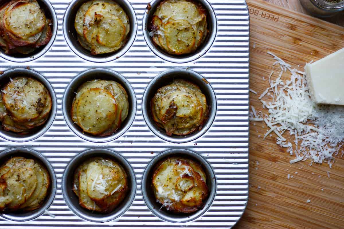 Cooked potato stacks still in the muffin tray. Some grated parmesan to the side.