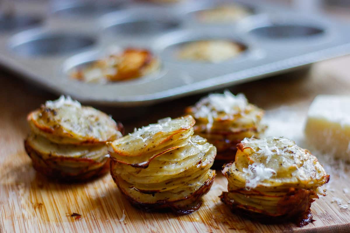 Crispy potato stacks set on wooden board with some finely grated parmesan cheese sprinkled over the top.