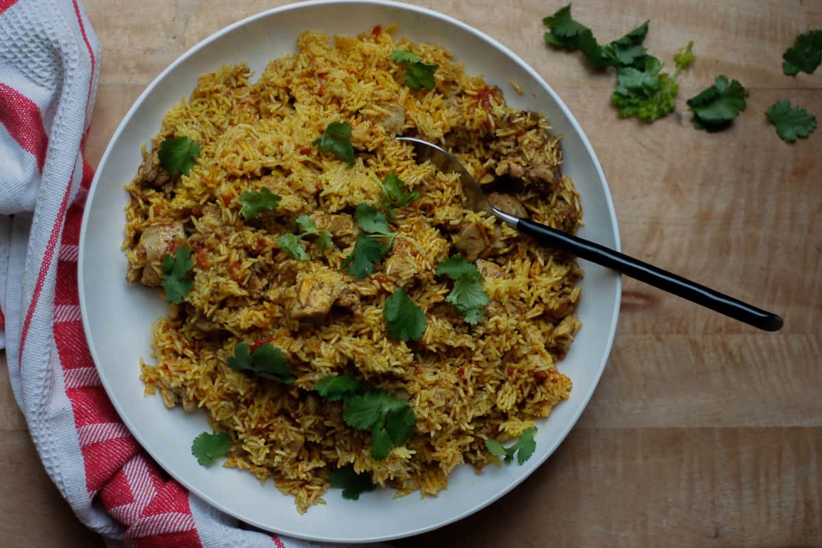 Bird's eye view of the finished pilau on a big white platter scattered with coriander leaves.