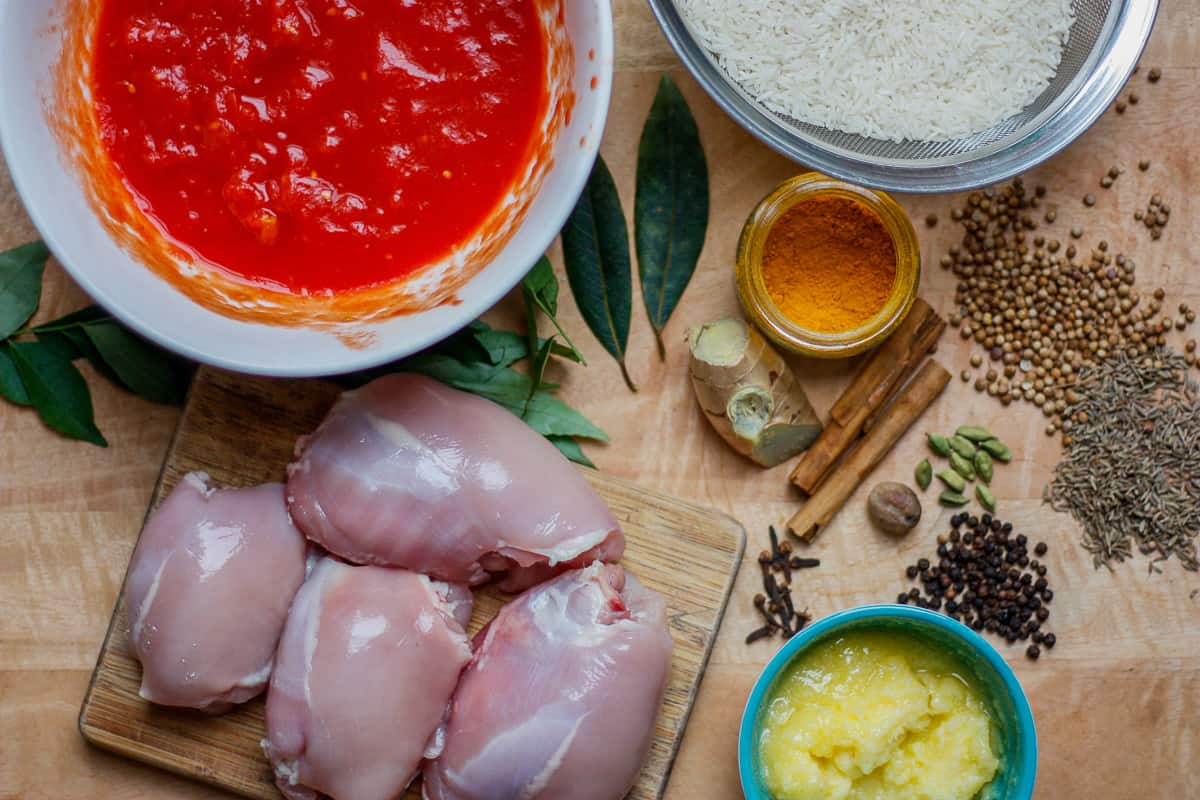 All the ingredients for Chicken Pilau laid out on a wooden work surface.