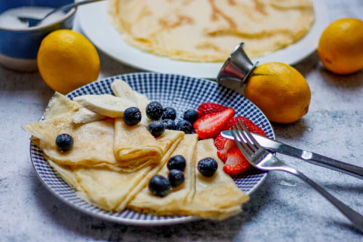 Folded up crepes on a blue plate with fresh fruit.