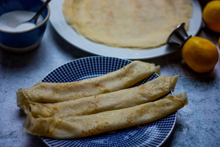 Three rolled- up pancakes sprinkled with sugar on a blue plate,