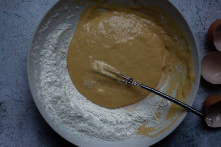 Flour being gradually combined with beaten eggs using a mini hand whisk