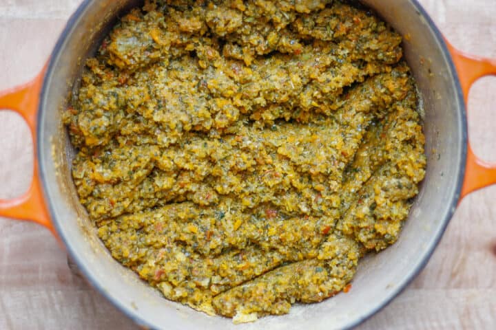 Bird's eye view of an orange casserole pot containing darkened and drier vegetable stock paste after cooking.