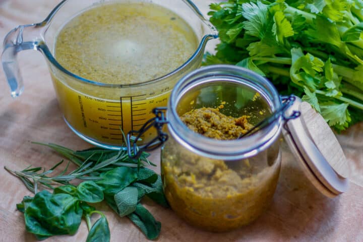 Glass jar containing vegetable stock paste. A glass measuring jug with made up stock in the background.