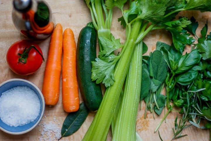 Ingredients for vegetable stock paste laid out on a wooden surface - vegetables, herbs and rock salt.