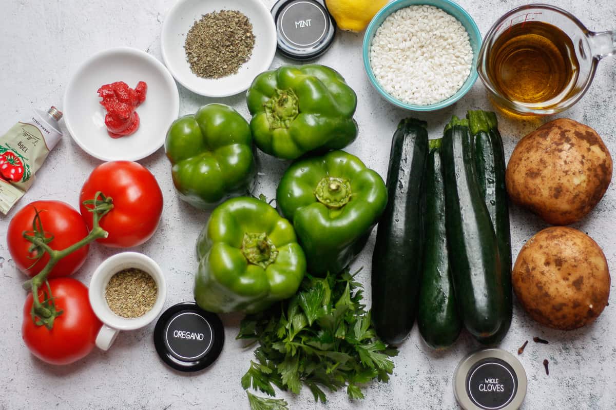 All the ingredients required to make gemista laid out on a stone surface.