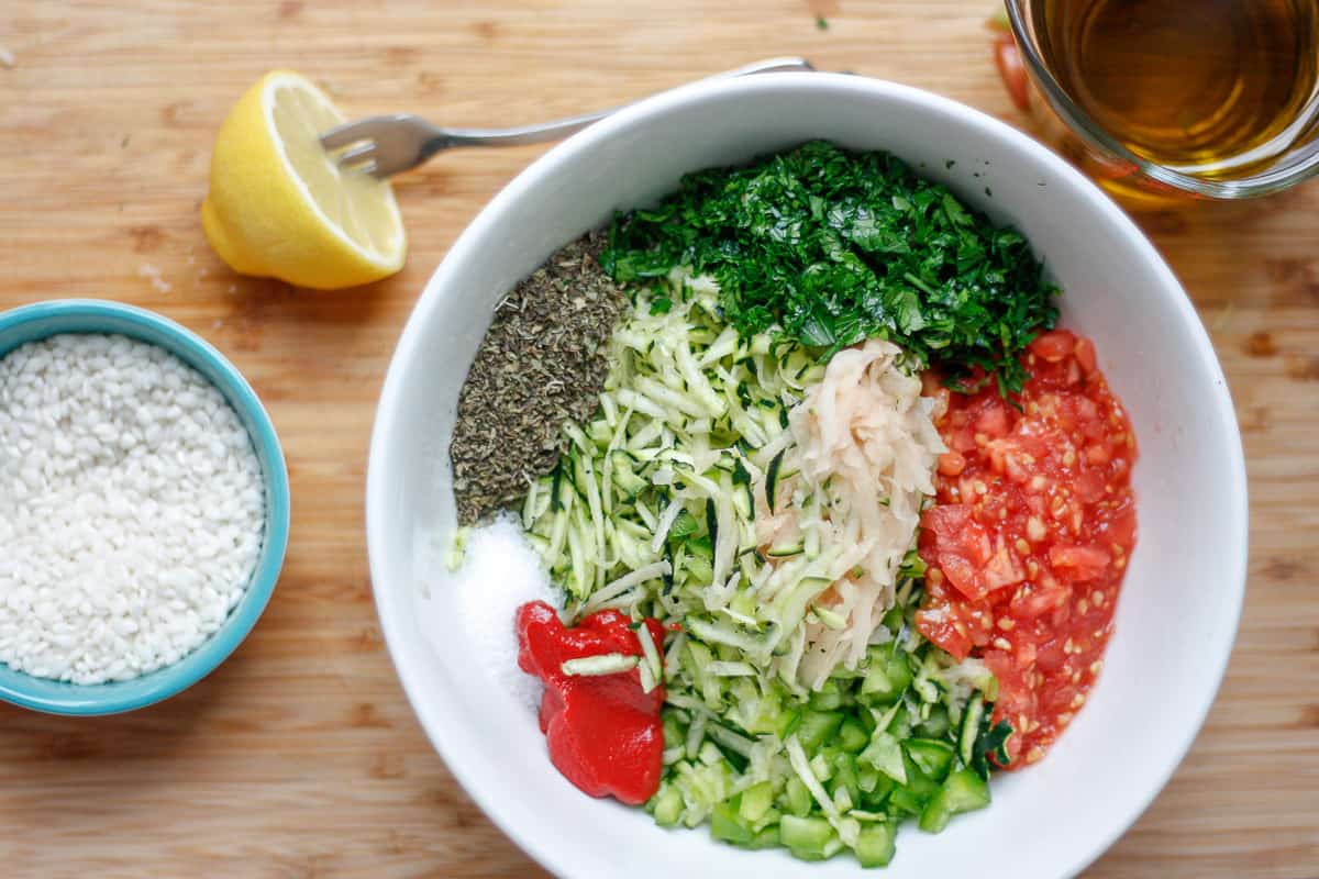 White bowl containing the gemista filling ingredients in separate piles. A small bowl of short-grain rice to the side.