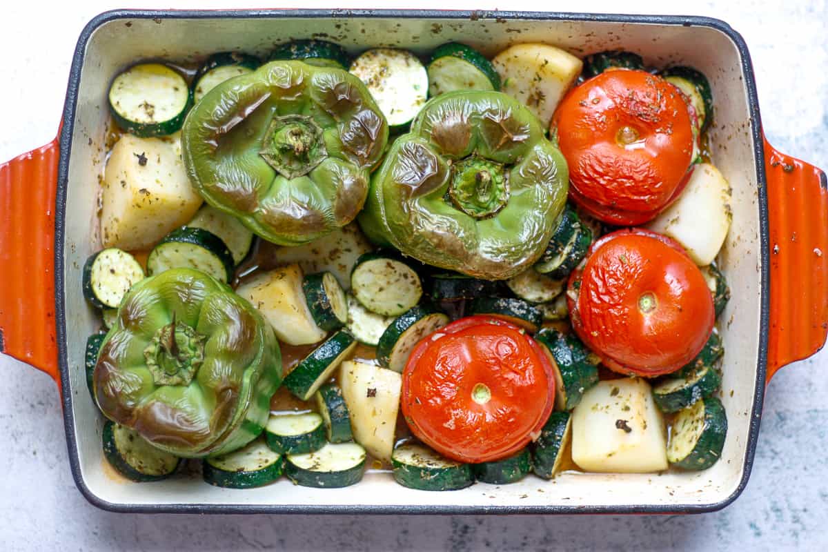 Bird's eye view of a roasting dish containing blistered whole tomatoes and green capsicum, potato chunks and zucchini discs.