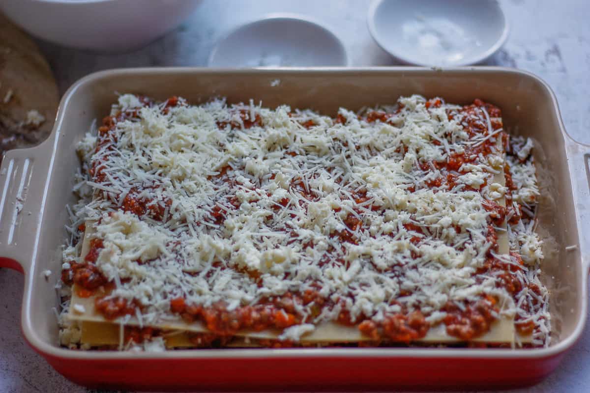 Assembled lasagna in a baking dish ready for covering for the oven. It is covered with a generous sprinkling of parmesan and mozzarella cheeses.