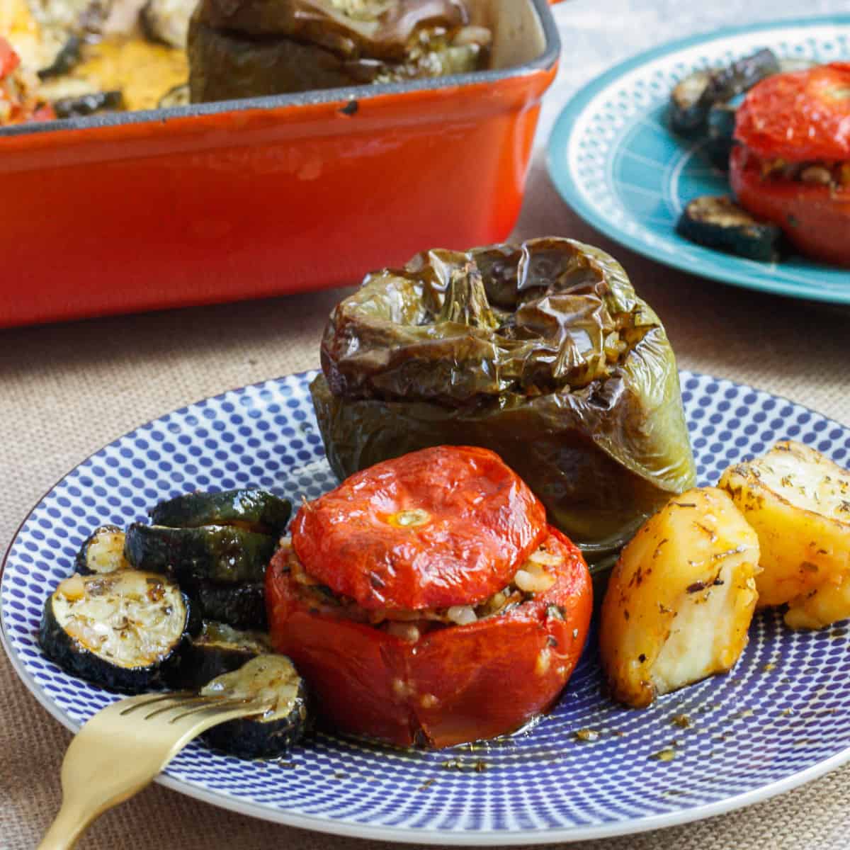 Stuffed tomato and capsicum with potato chunks and zucchini discs on a blue patterned plate.