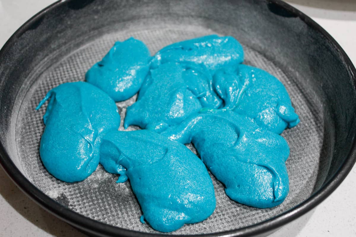 Blobs of blue batter in a cake pan ready to be spread into an even layer and baked. It's a small amount to make a thin layer.