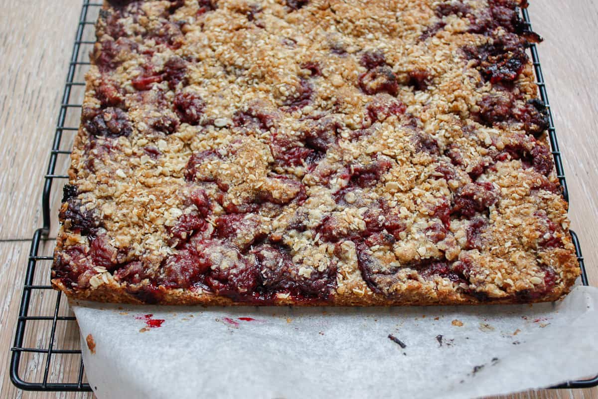 Whole uncut raspberry slice on baking paper on a cooling rack.